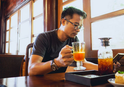 Man using phone while holding drink in glass on table at restaurant