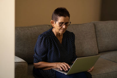 Smiling senior woman sitting at home office workplace looking in laptop.