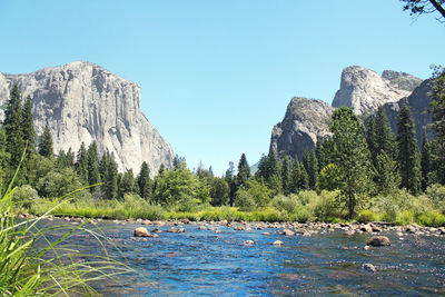 River and rocky mountains against clear sky on sunny day