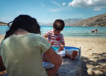 Siblings drawing while sitting on lounge chair at beach