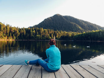 Rear view of woman sitting on pier over lake against sky