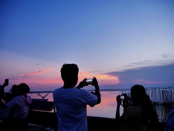 People photographing sea against sky during sunset