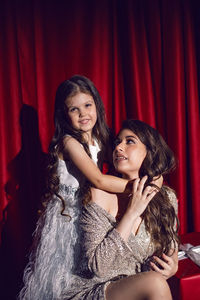 Beautiful young woman in a shiny dress is sitting with a daughter child on red gift boxes with bows 