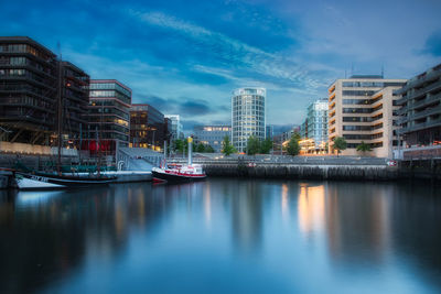 Boats moored in river by buildings against sky in city