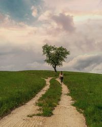 Rear view of person walking on road amidst field against sky