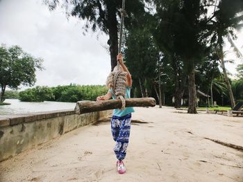 Full length of girl walking with rope swing on sand 