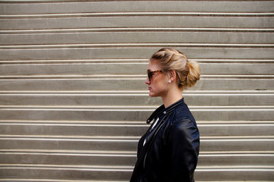 Side view of a young woman standing against shutter