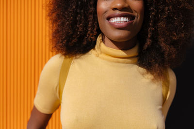 Portrait of a curly haired black woman looking at camera in front of a yellow background