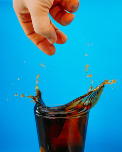 Cropped hand of woman holding drink against blue background