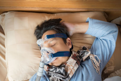 High angle view of mature man wearing oxygen mask while sleeping on bed