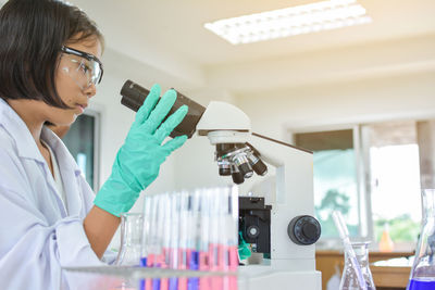 Female scientist using microscope at table in laboratory