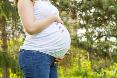 Midsection of pregnant woman standing against trees