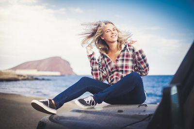 Beautiful young woman sitting on beach against sky