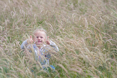 Portrait of happy girl in field showing thumbs up