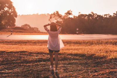 Rear view of woman standing on field against sky during sunset