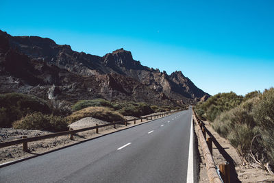 Empty road by mountain against clear sky