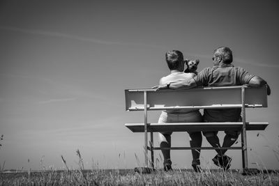 Couple sitting on seat in field against sky