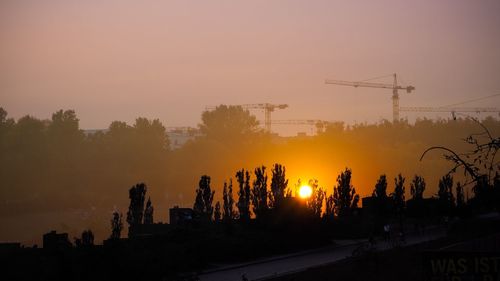 High angle view of road by silhouette trees and cranes against sky during sunset