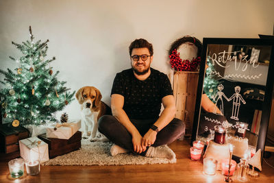 Portrait of man with dog sitting at home during christmas