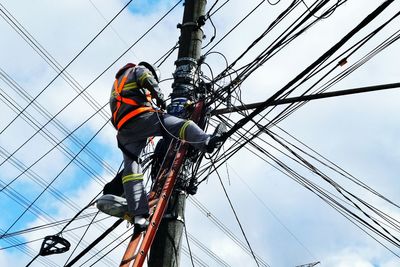 Low angle view of electrician working on pole against cloudy sky