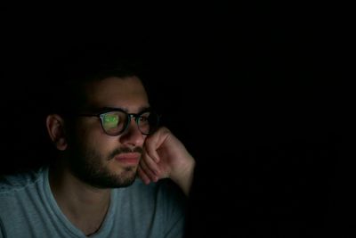 Close-up of young man wearing eyeglasses against black background