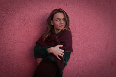 Young woman looking away while standing against pink wall