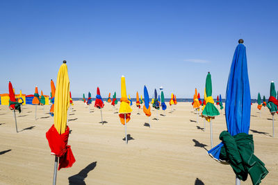 Closed beach umbrellas at beach against blue sky