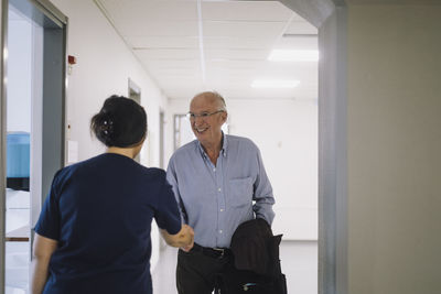 Smiling senior male patient shaking hand with female medical staff at hospital