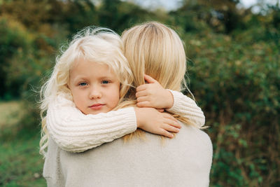 A little blond girl in her mother's arms hugs her neck.