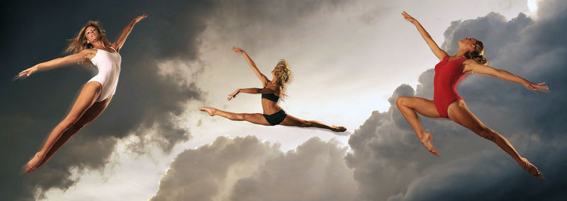 Low angle view of dancers jumping in mid-air against cloudy sky