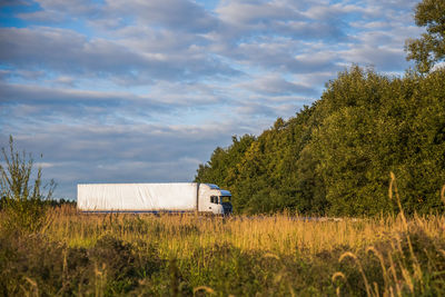 Truck on grassy field by trees against sky