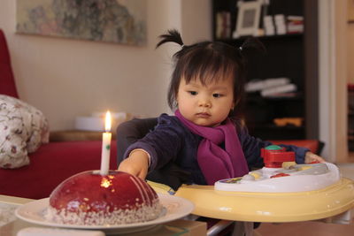 Cute girl sitting in baby walker by cake