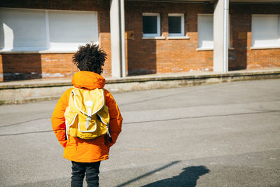 Rear view of schoolboy standing on street during sunny day