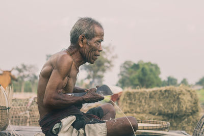 Side view of shirtless man sitting against clear sky