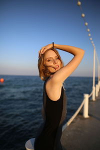 Young blonde woman standing by sea against sky