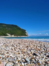 Surface level of stones on beach against clear blue sky