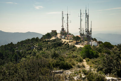 Electricity pylons by trees on mountain against sky