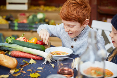 Happy male and female siblings having soup at back yard table