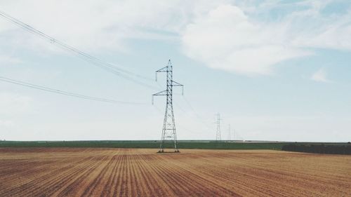 Electricity pylon on field against cloudy sky