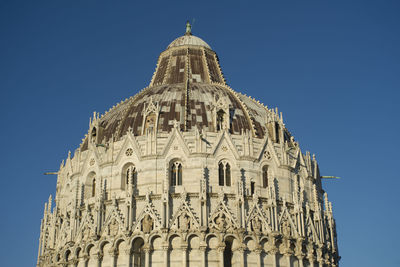 Low angle view of pisa baptistery against clear blue sky in city