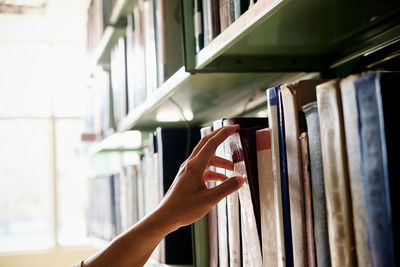 Cropped hand of woman removing book from bookshelf in library