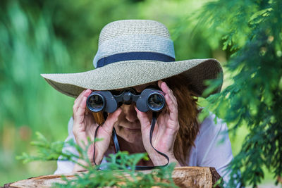 Woman wearing hat looking through binoculars in forest