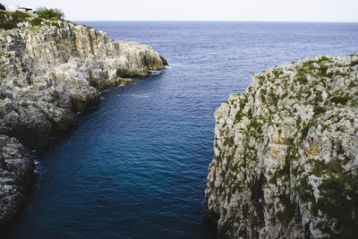 Idyllic shot of rock formations in sea against sky