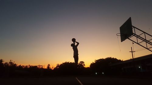 Silhouette man playing basketball against sky during sunset