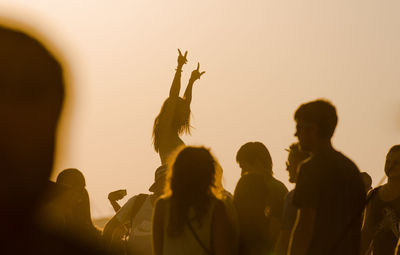 People looking at woman dancing at beach during sunset