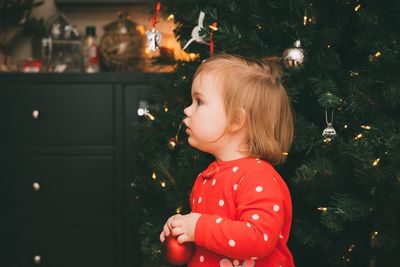 Cute girl looking away against christmas tree at home