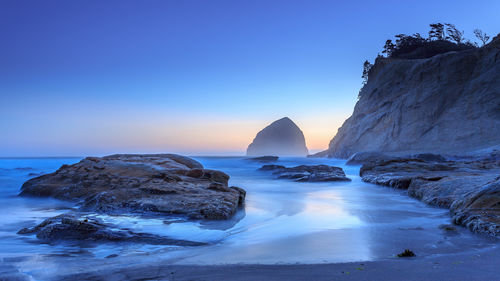 Rocks in sea against clear sky during sunset