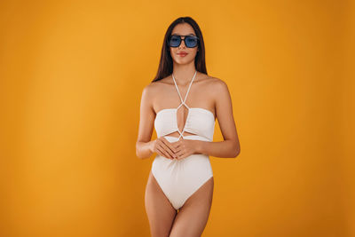 Portrait of young woman wearing sunglasses against yellow background