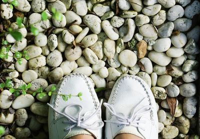 Low section of person wearing white shoes standing on pebbles