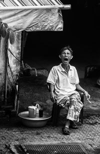 Full length of man yawning while sitting on chair at footpath